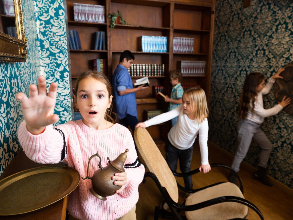 Interested tween girl trying to reach for some item in escape room stylized as old library, holding out her hand