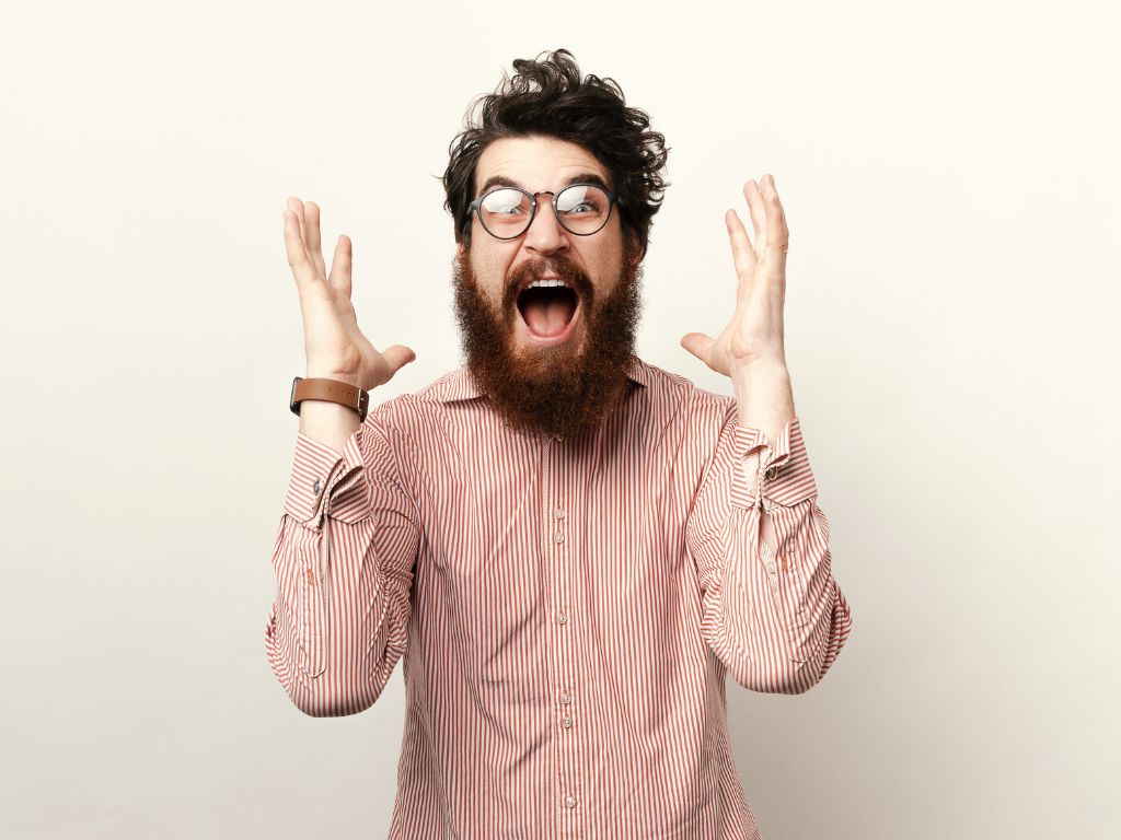 Thrilled excited attractive bearded man in glasses screaming and gesturing with raised palms