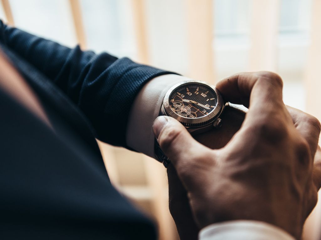 a stylish mechanical watch on the arm of a man dressed in a blue jacket with a white shirt that watches the time on the clock holding the clock by hand