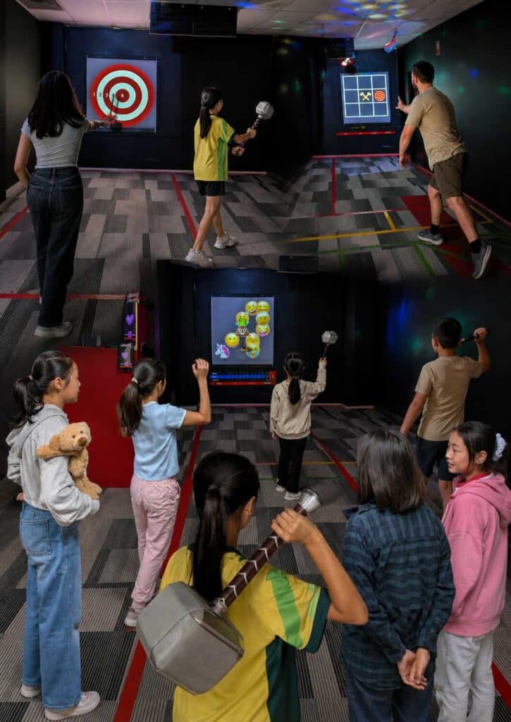 Group of kids, teens, and adults enjoying Entermission’s exclusive hammer throwing challenge room, Australia’s first interactive axe and hammer throwing experience. Players take turns throwing soft-tipped hammers at digital targets in a modern indoor arena with marked lanes and illuminated game screens, creating a fun, safe, and family-friendly activity unique to Entermission.